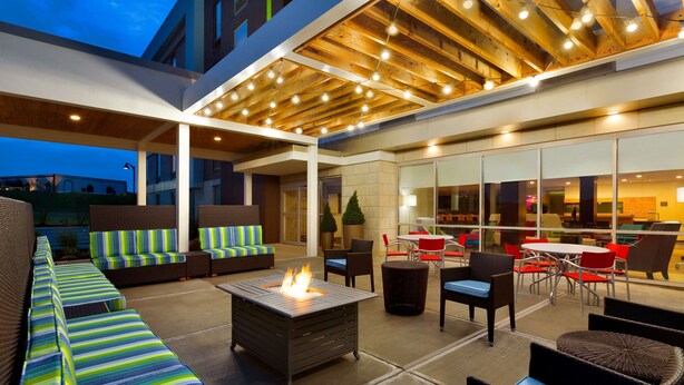 An outdoor seating area with a fire pit, cushioned seating, and a covered patio with wooden beams and string lights.