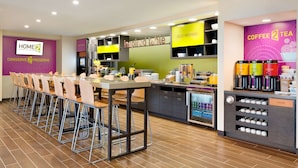 A modern hotel kitchen with a long dining table, bar stools, and a coffee station.