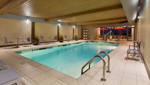 An indoor swimming pool with a wooden ceiling, tiled floor, and seating areas with tables and chairs.