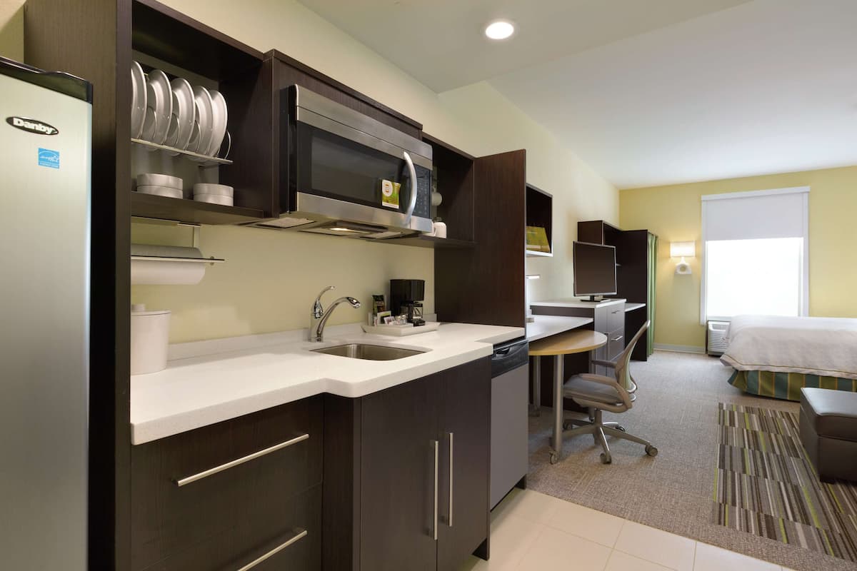 Habitación de hotel compacta con kitchenette, escritorio y cama.