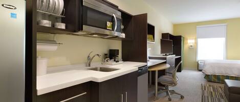 A compact hotel room with a kitchenette, a desk, and a bed.