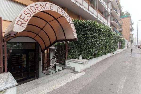 Un immeuble avec une enseigne indiquant « RÉSIDENCE DESENZANO » et un escalier menant à l’entrée.