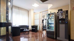 A hotel lobby with a seating area, a vending machine, and a glass door leading to another room. - Residence Desenzano (Milan)
