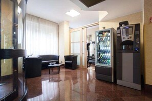 A hotel lobby with a seating area, a vending machine, and a glass door leading to another room. - Residence Desenzano (Milan)