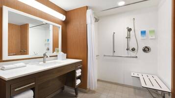 A modern bathroom with a wooden vanity, a large mirror, a shower with a handheld showerhead, and a bench.