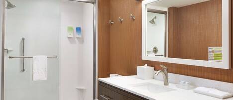Une salle de bain moderne avec une douche à l’italienne en verre, des toilettes blanches, un meuble-lavabo en bois doté d’un grand miroir et un lavabo blanc.
