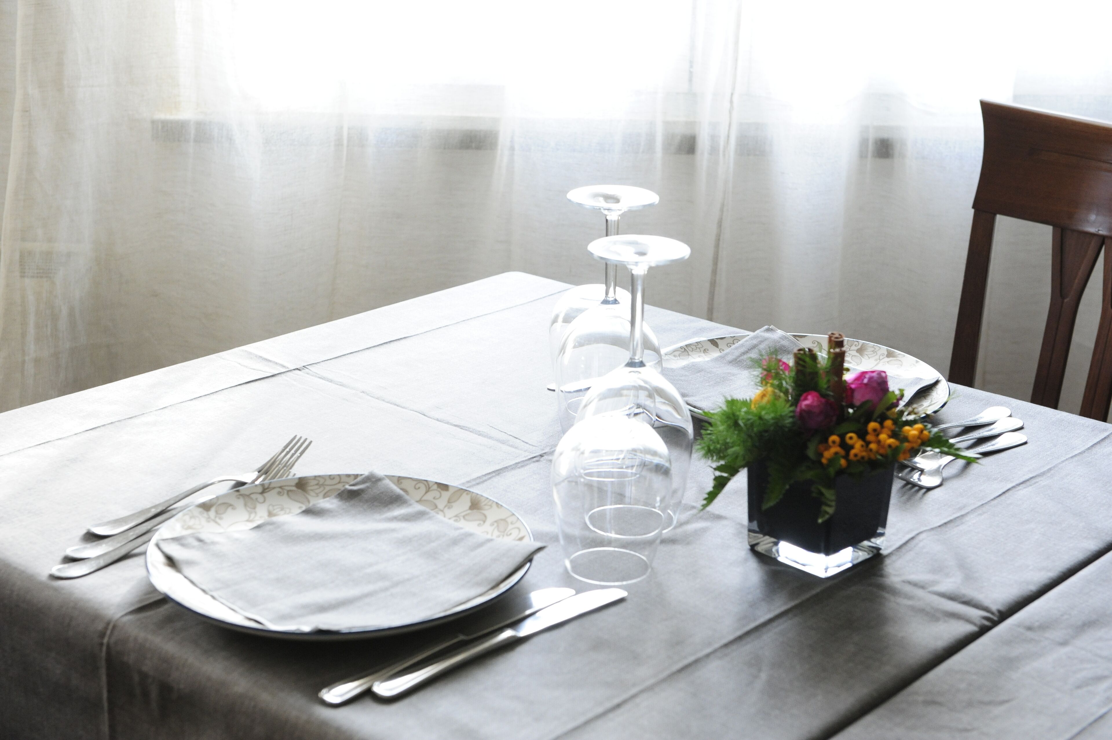 A table set for dining with plates, cutlery, glasses, and a vase with flowers.