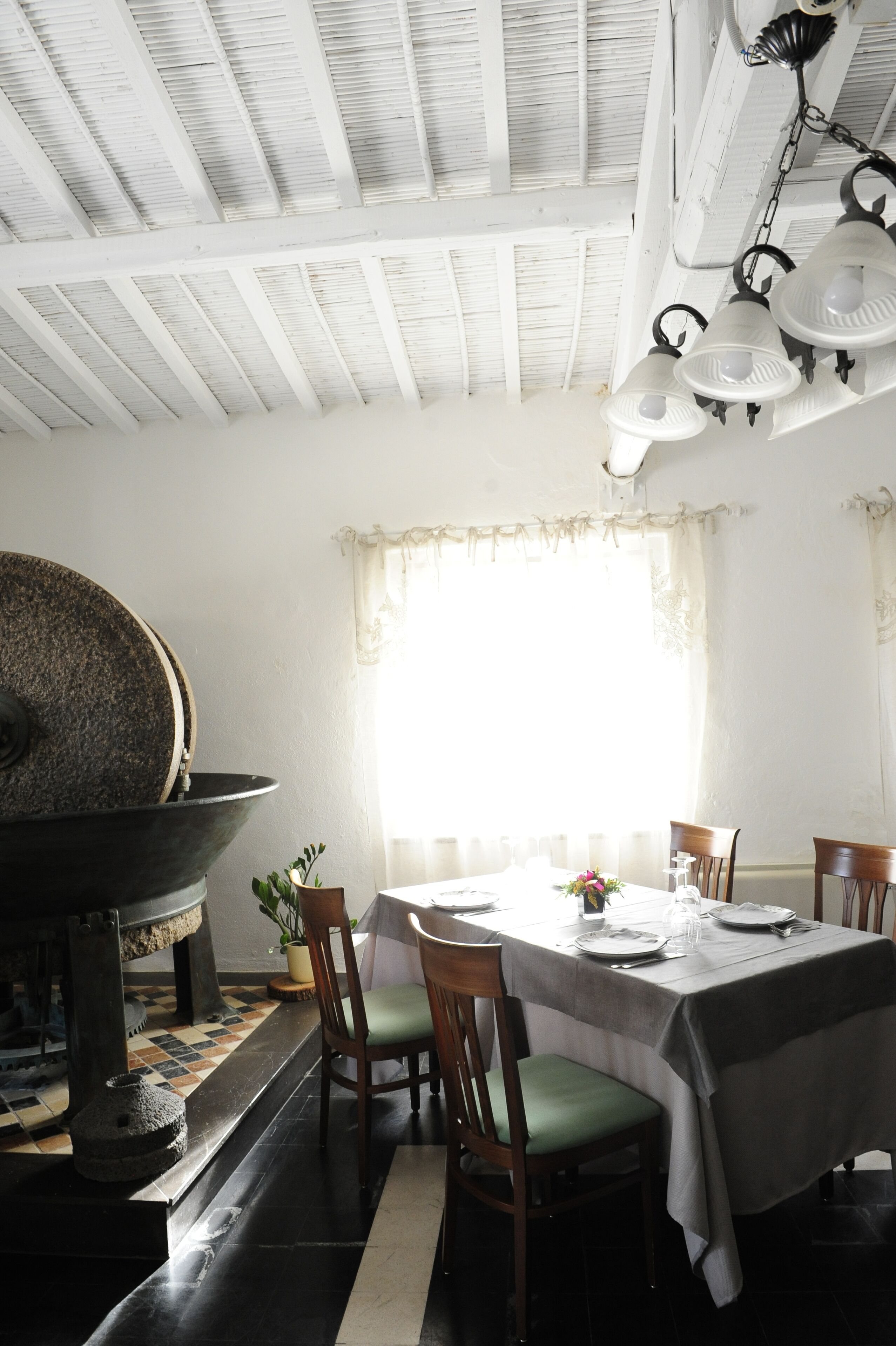 A dining area with a table set for four, wooden chairs, a large window with curtains, and a ceiling with exposed beams.
