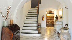A spacious hallway with a staircase, a wooden dresser, a vase with dried flowers, and a checkered floor. - Sa Mola (Bonarcado)