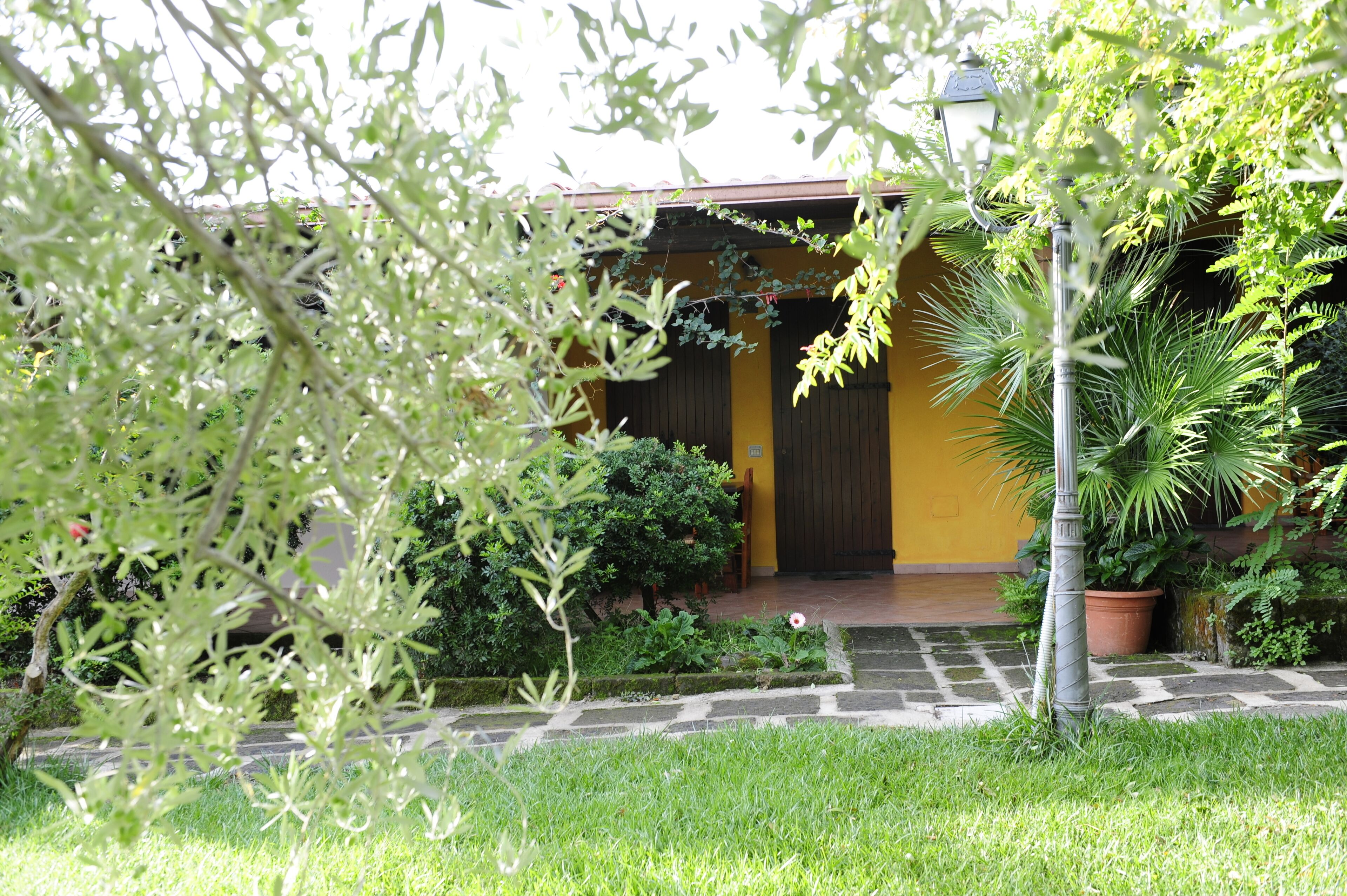A yellow building with a dark door, surrounded by lush greenery and a stone pathway.