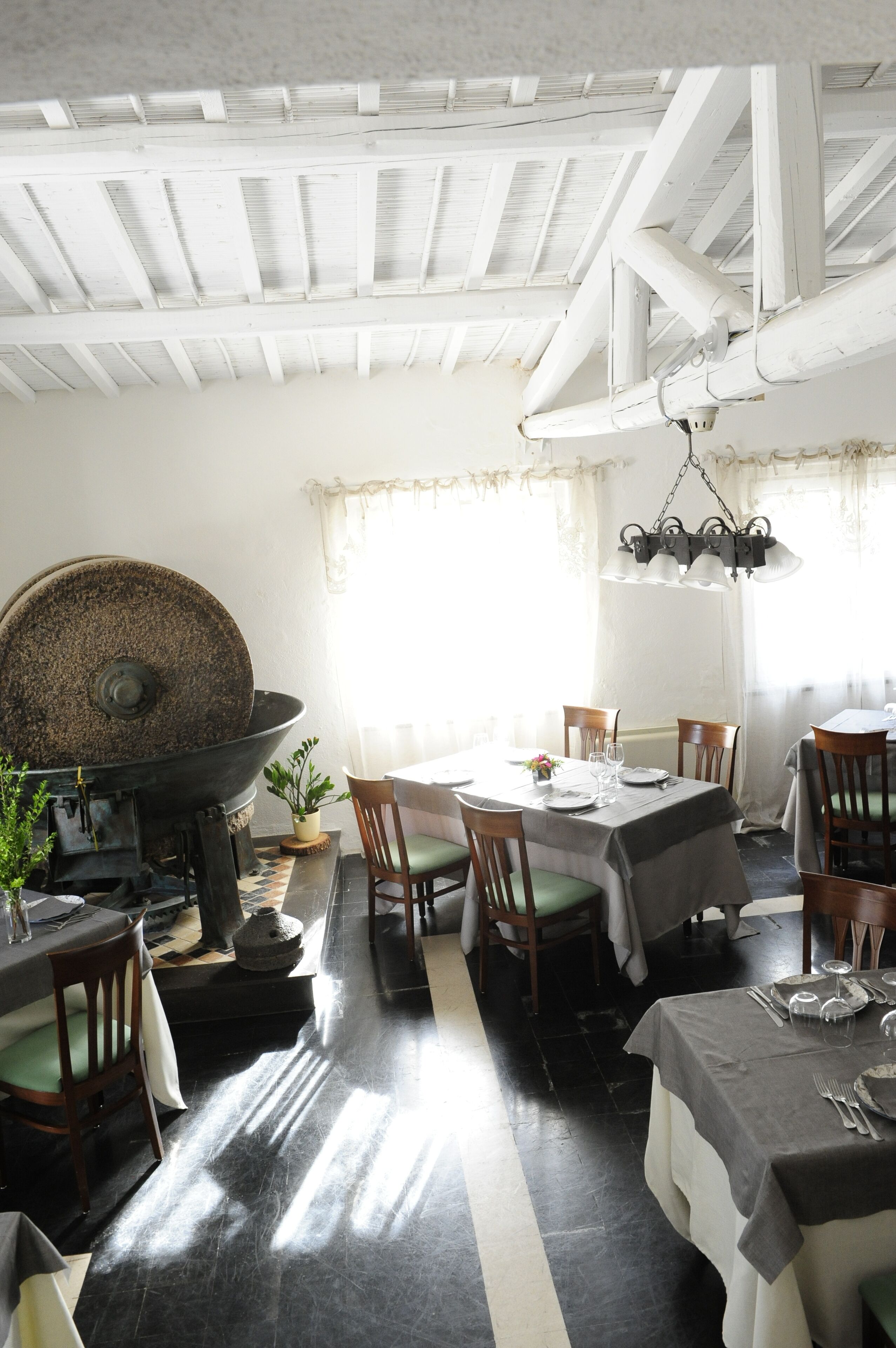 A dining area with a large stone mill, wooden chairs, and a table set for four.