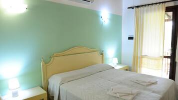 A neatly made bed with a white comforter and folded towels, a bedside lamp, and a nightstand.
