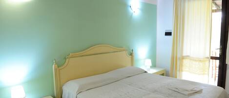 A neatly made bed with a white comforter and folded towels, a bedside lamp, and a nightstand.