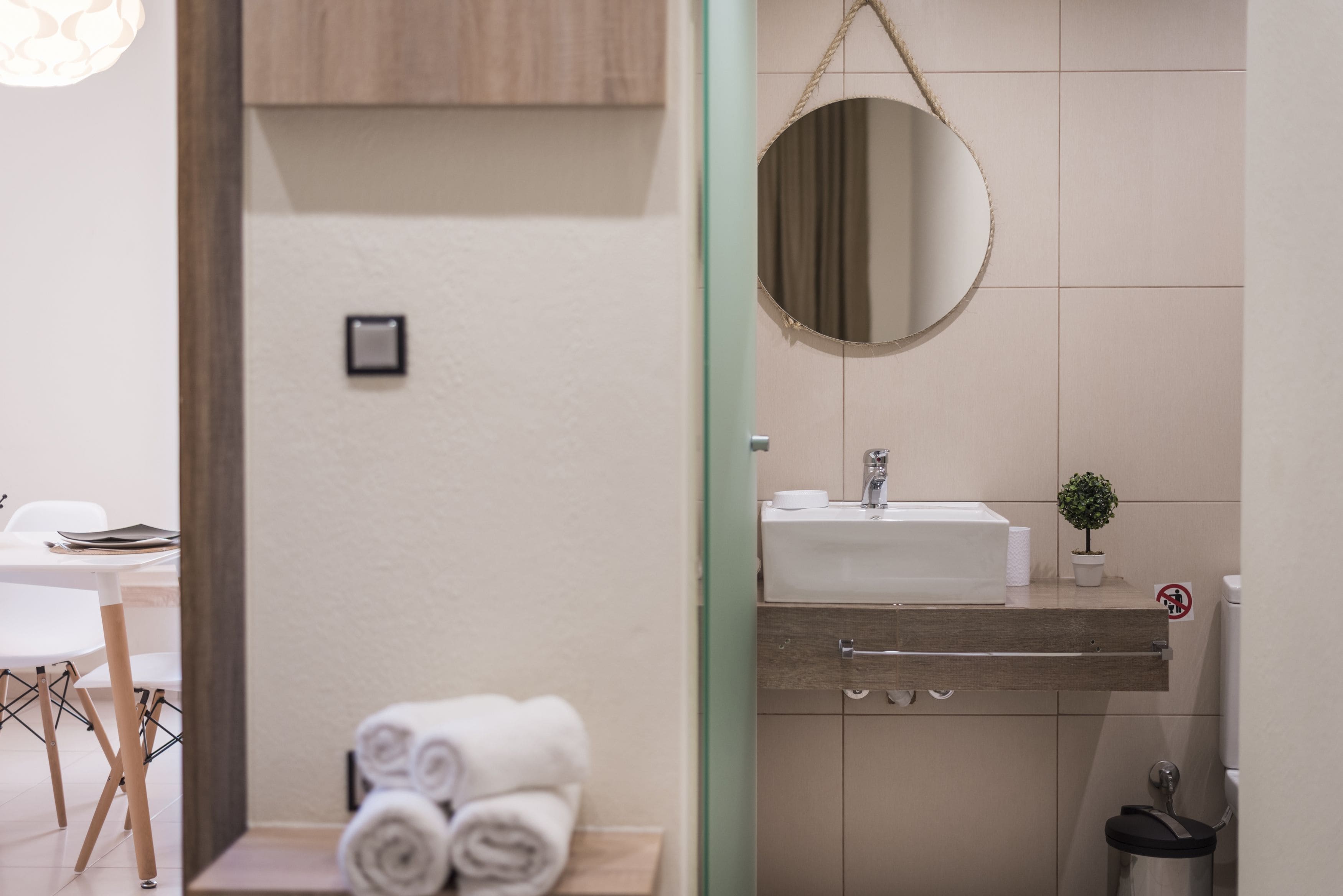 A modern bathroom with a round mirror, white sink, and a small potted plant.