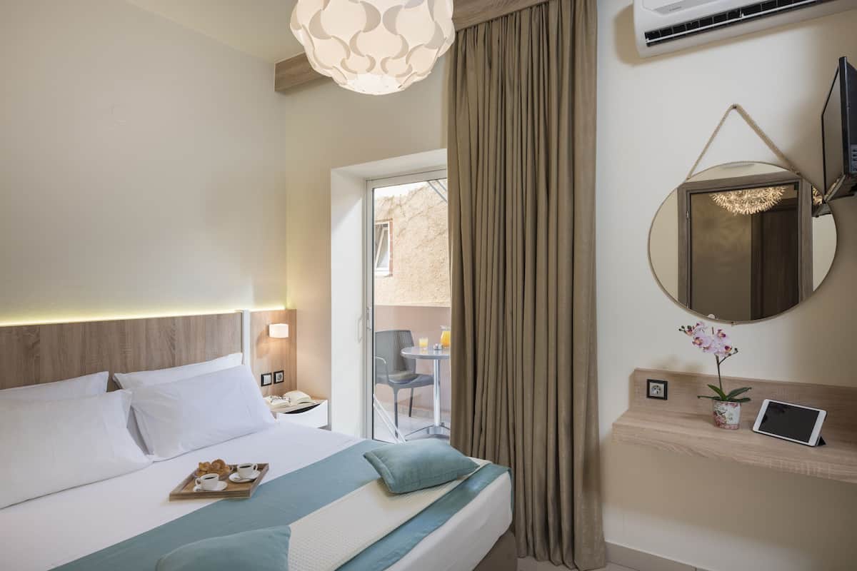 Quarto de hotel com cama, mesa de cabeceira, luminária, TV e vista para o exterior.