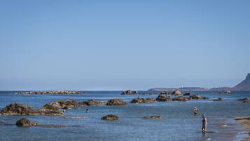A beach with clear blue water and rocky outcrops.