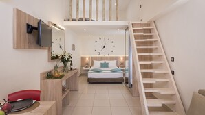 A modern bedroom with a large bed, a TV mounted on the wall, a desk with a computer, and a staircase leading to an upper level. - Sea & City Apartments (Chania)