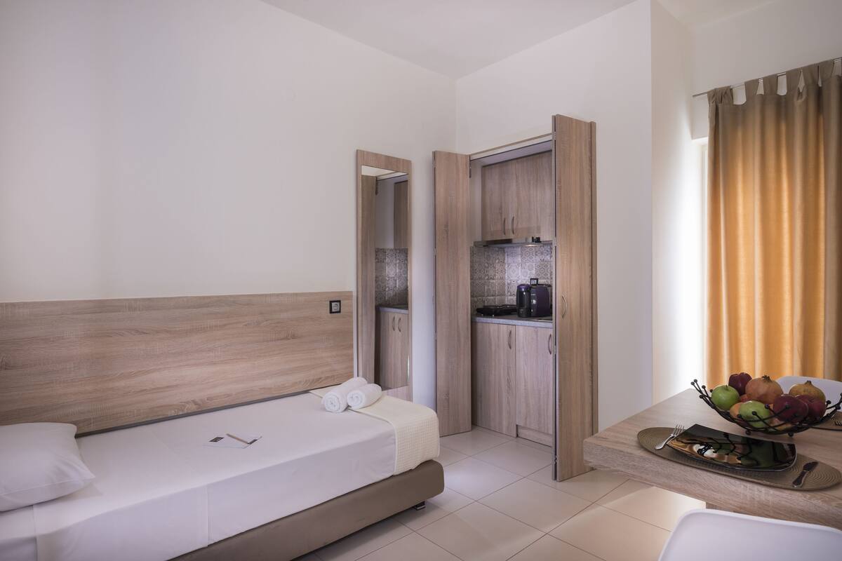Quarto de hotel moderno com uma cama, uma kitchenette pequena e um espaço de jantar com uma fruteira.