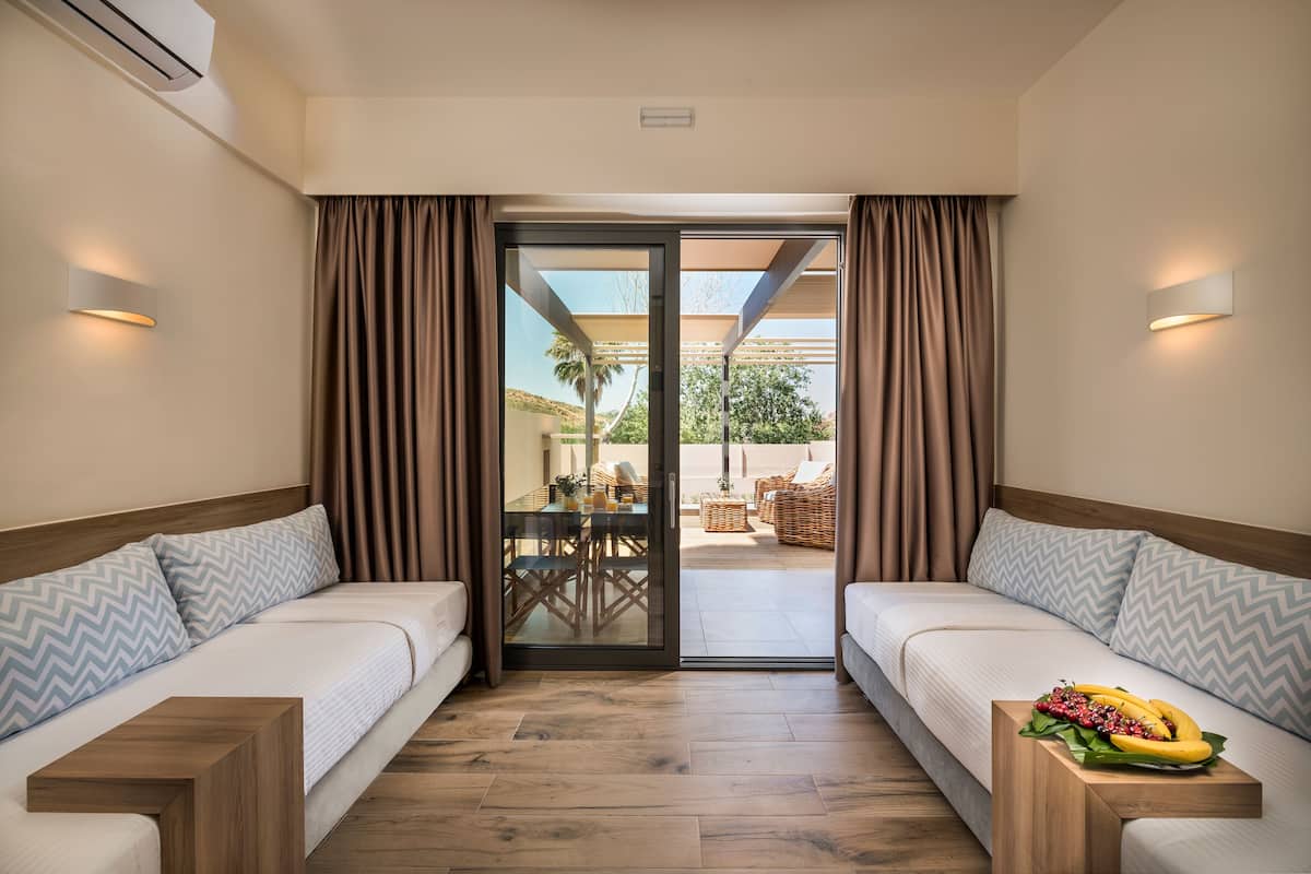Quarto de hotel com duas camas, porta de vidro que dá para uma área externa com mesa e chão de madeira.