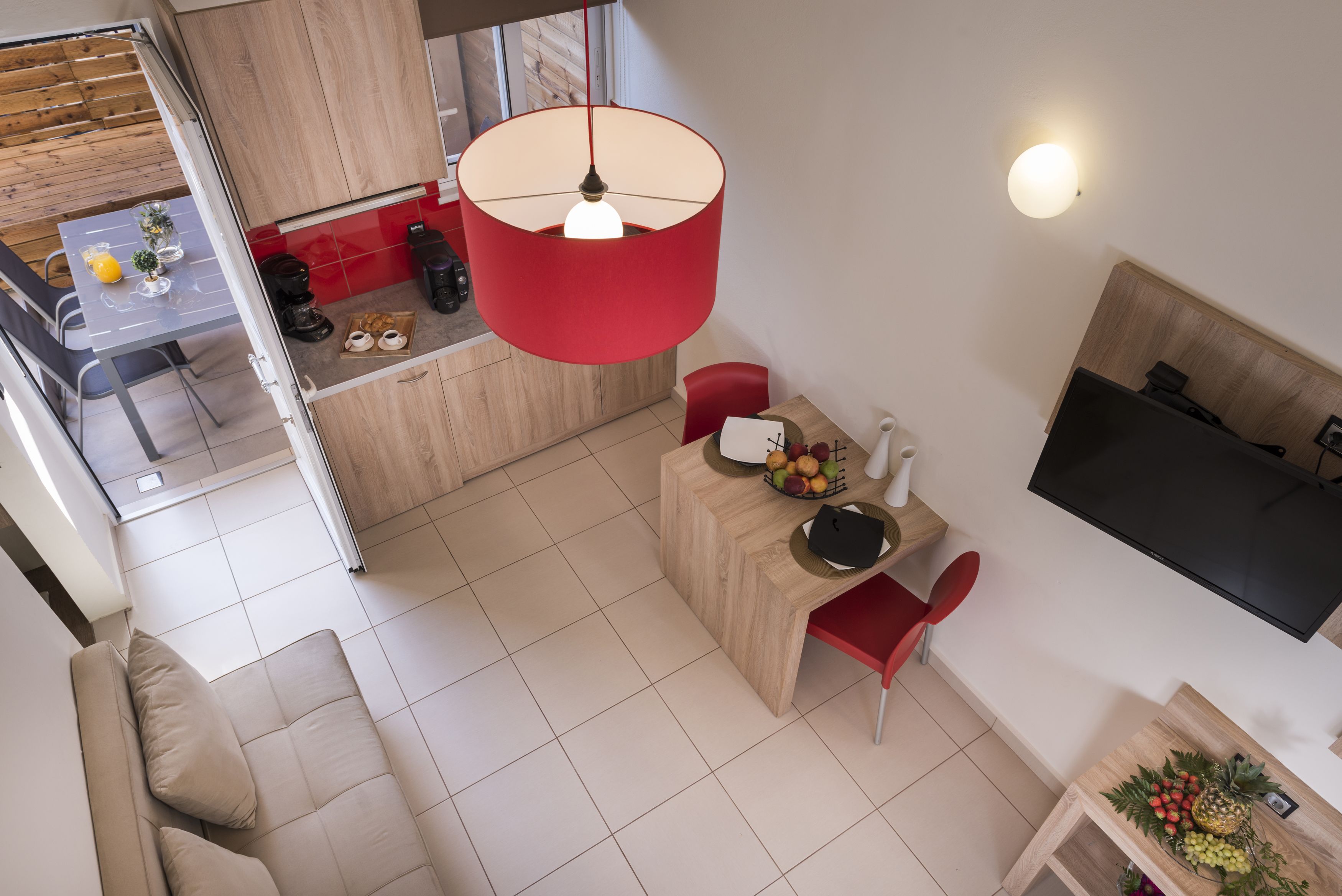 A modern living space with a dining area, a sofa, a TV, and a kitchen visible through an open door.