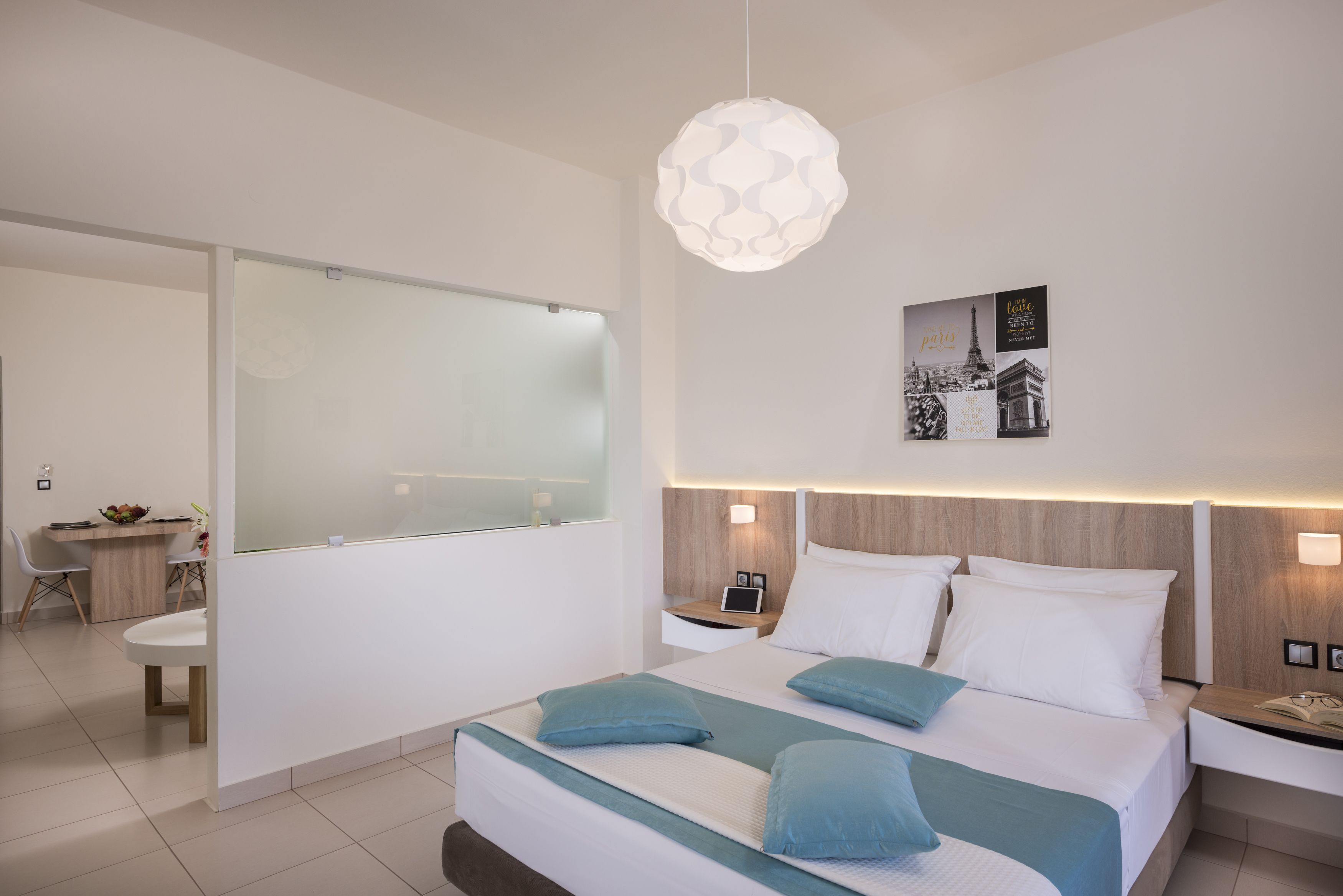Een moderne hotelkamer met een groot bed, nachtkastjes, een bureau en een glazen scheiding.