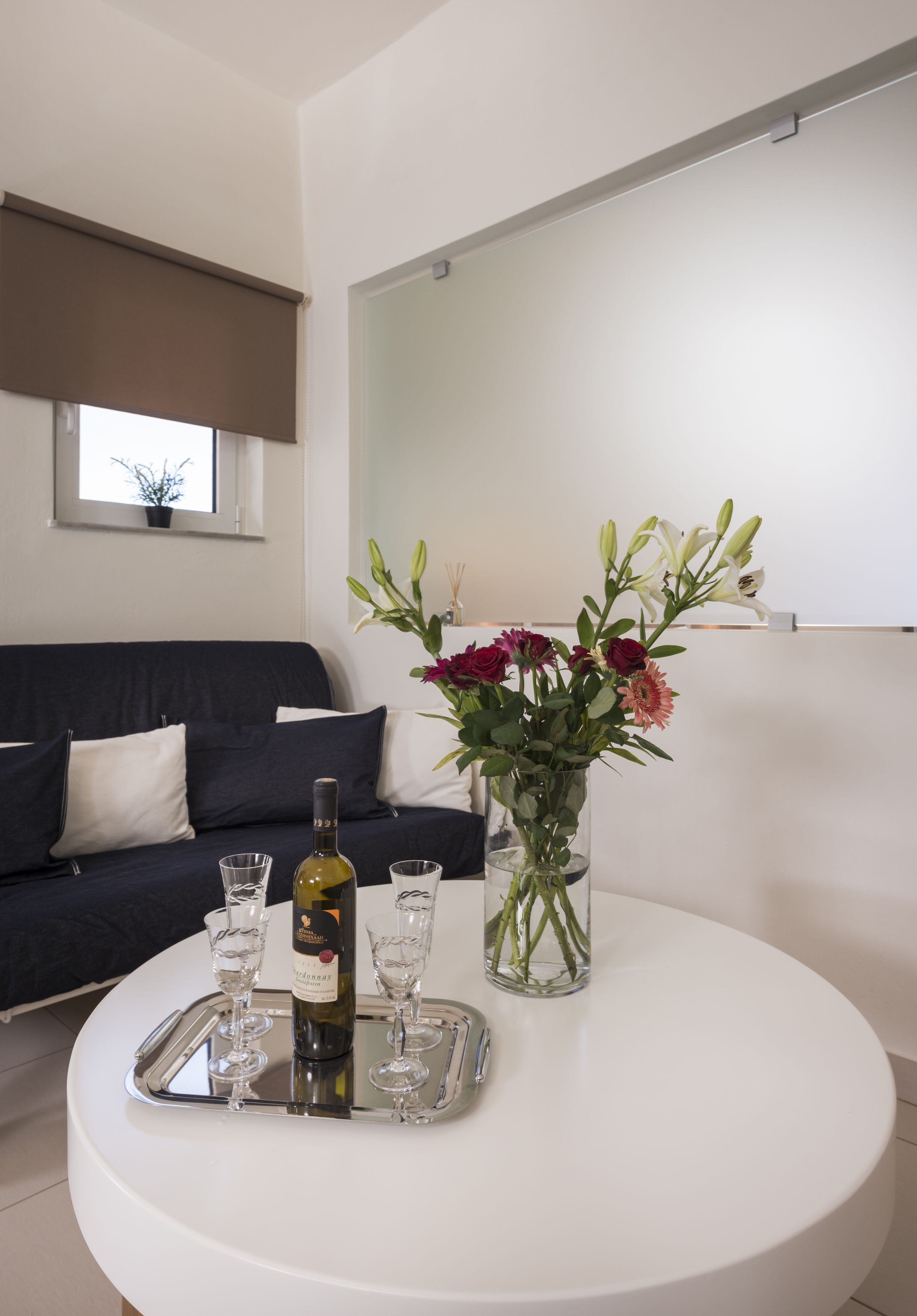 Ein modernes Wohnzimmer mit einem dunkelgrauen Sofa, einem weißen Couchtisch, einer Blumenvase und einer Weinflasche.