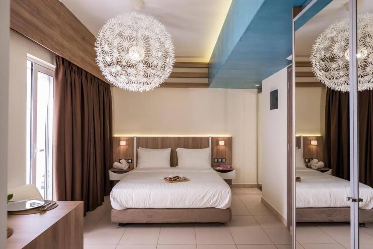 Quarto de hotel moderno com uma cama grande, mesas de cabeceira, um espelho e luminárias decorativas no teto.