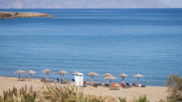 A beach with sun loungers and umbrellas, a white structure, and mountains in the background. - Sea & City Apartments (Chania)