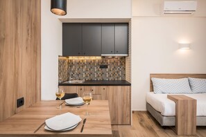 A compact kitchen with dark cabinets, a tiled backsplash, and a dining area with a wooden table set for two. - Sea & City Apartments (Chania)