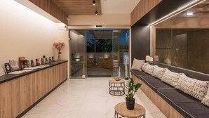 A modern reception area with a wooden reception desk, a seating area with patterned cushions, and a glass door leading to a balcony. - Sea & City Apartments (Chania)