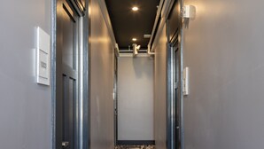 A narrow hallway with a patterned carpet, doors on both sides, and a light switch on the wall. - Hotel 32One (San Francisco)