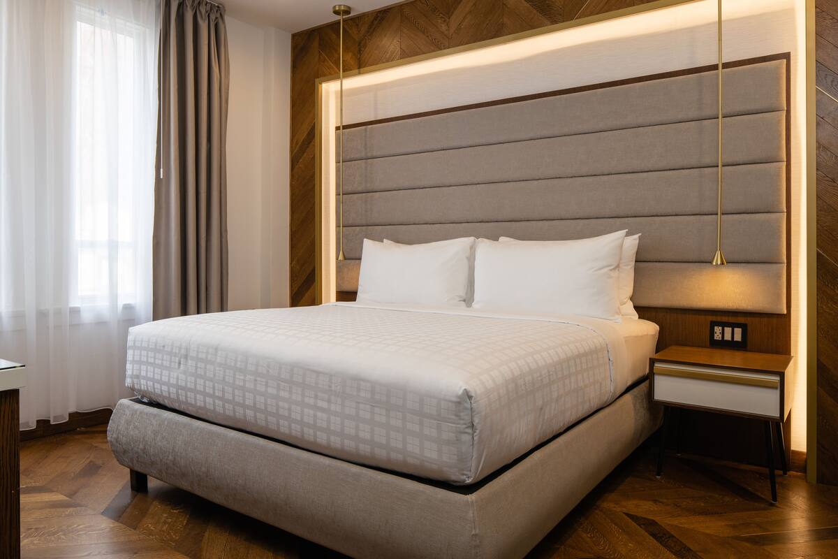 Una habitación de hotel moderna con una cama grande, una mesita de noche y otra mesita auxiliar.