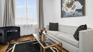 A modern living room with a sofa, a coffee table, and a large window with curtains. - Hotel 32One (San Francisco)