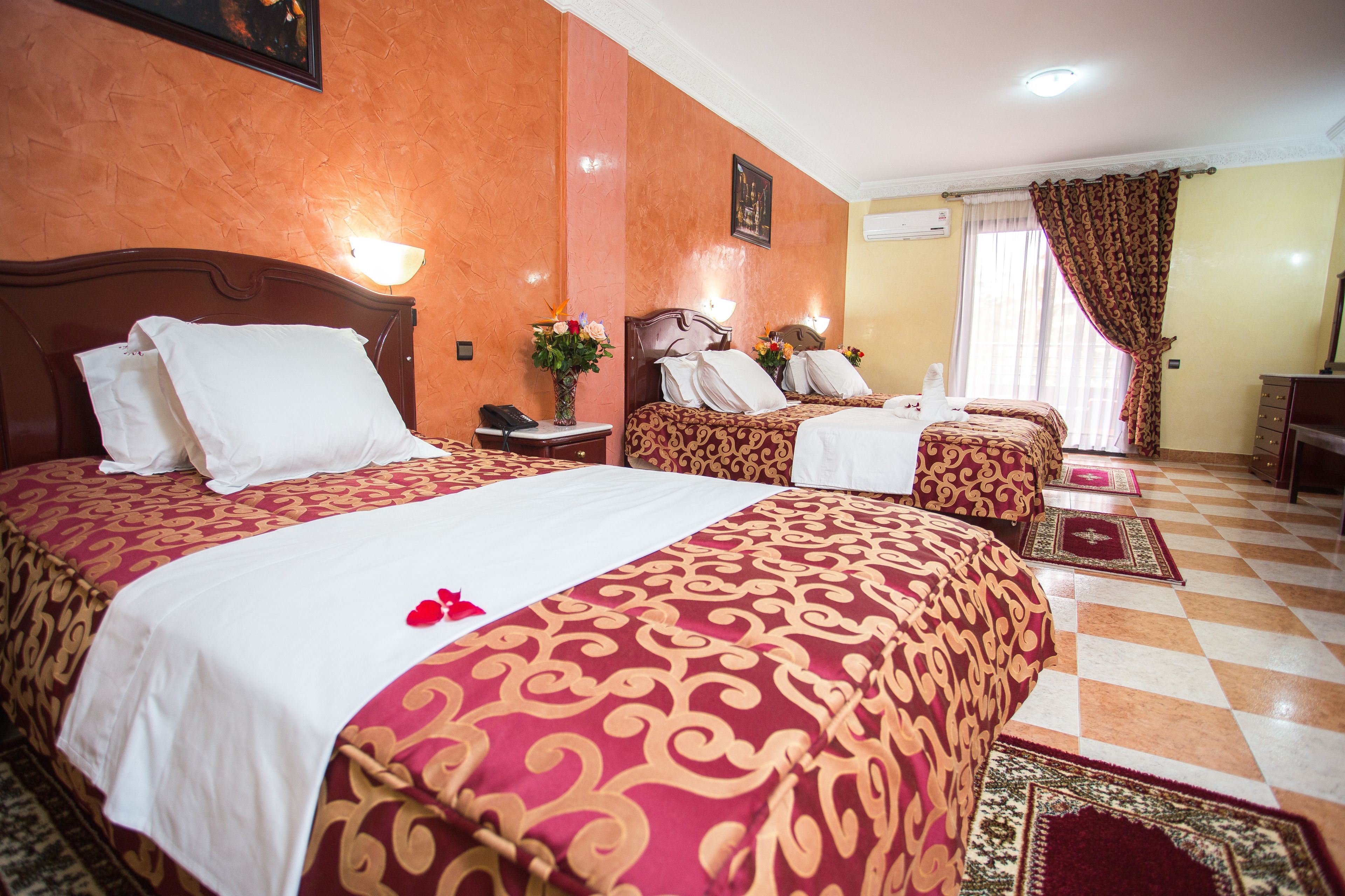 A hotel room with two beds, a checkered floor, and a large window with curtains.
