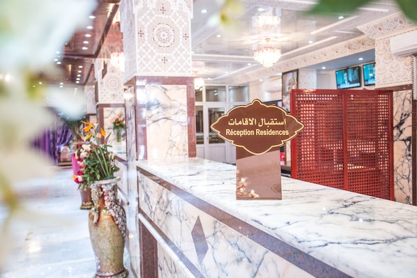 A reception desk with a marble countertop, a sign indicating 'Reception Residences', and a red partition in the background.
