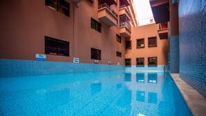 A swimming pool with a tiled floor, surrounded by a building with balconies and windows.