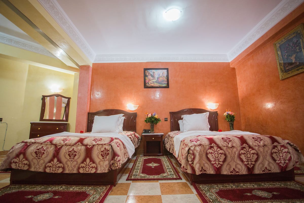 Una habitación de hotel con dos camas, una mesita de noche, un espejo y un cuadro en la pared.
