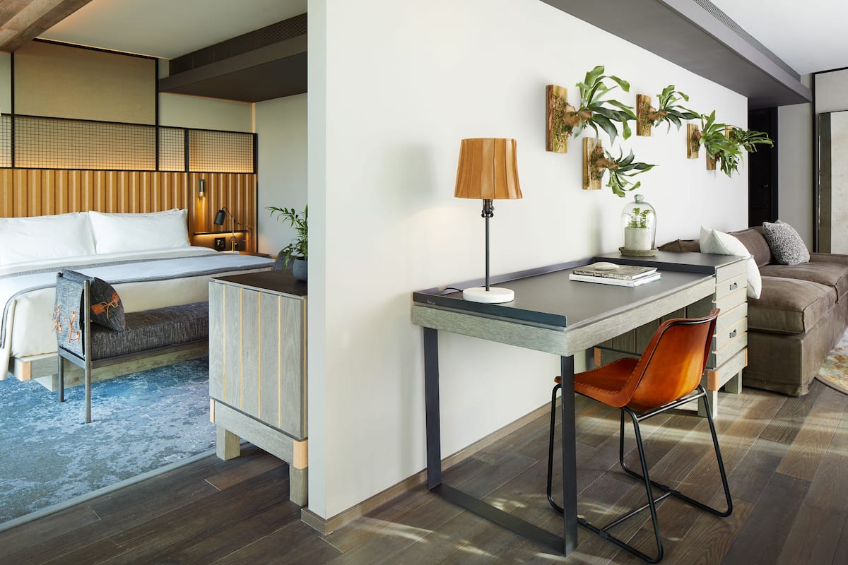 A modern hotel room with a bed, desk, and seating area.