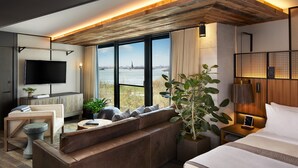 Habitación de hotel moderna con un ventanal que ofrece vistas a un cuerpo de agua y una estatua distante.