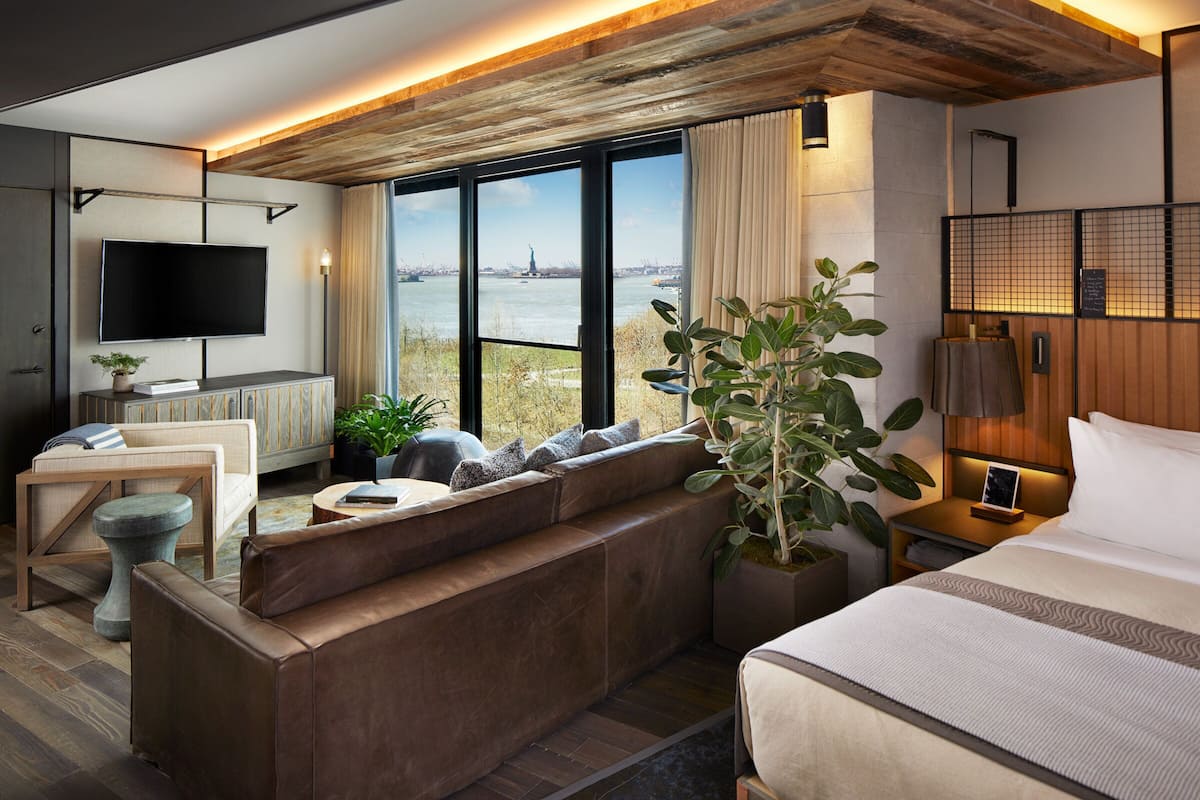 A modern hotel room with a large window offering a view of a body of water and a distant statue.