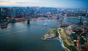 An aerial view of a cityscape with a prominent bridge, a river, and a waterfront area with buildings and greenery.