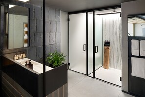 A modern bathroom with a large mirror, a black sink, and a potted plant.