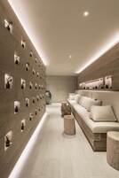 A modern interior with a long, narrow hallway, a sofa with cushions, and a wall with multiple small windows.
