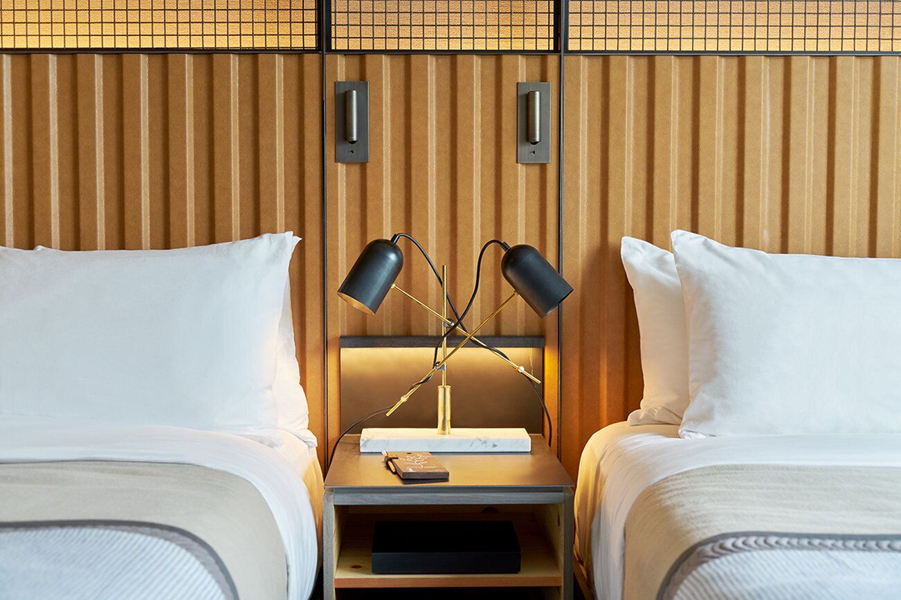 A hotel room with two beds, a nightstand with a lamp, and a wooden headboard.