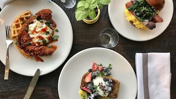 A table with three plates of food, a fork, a knife, a glass of water, and a small potted plant.