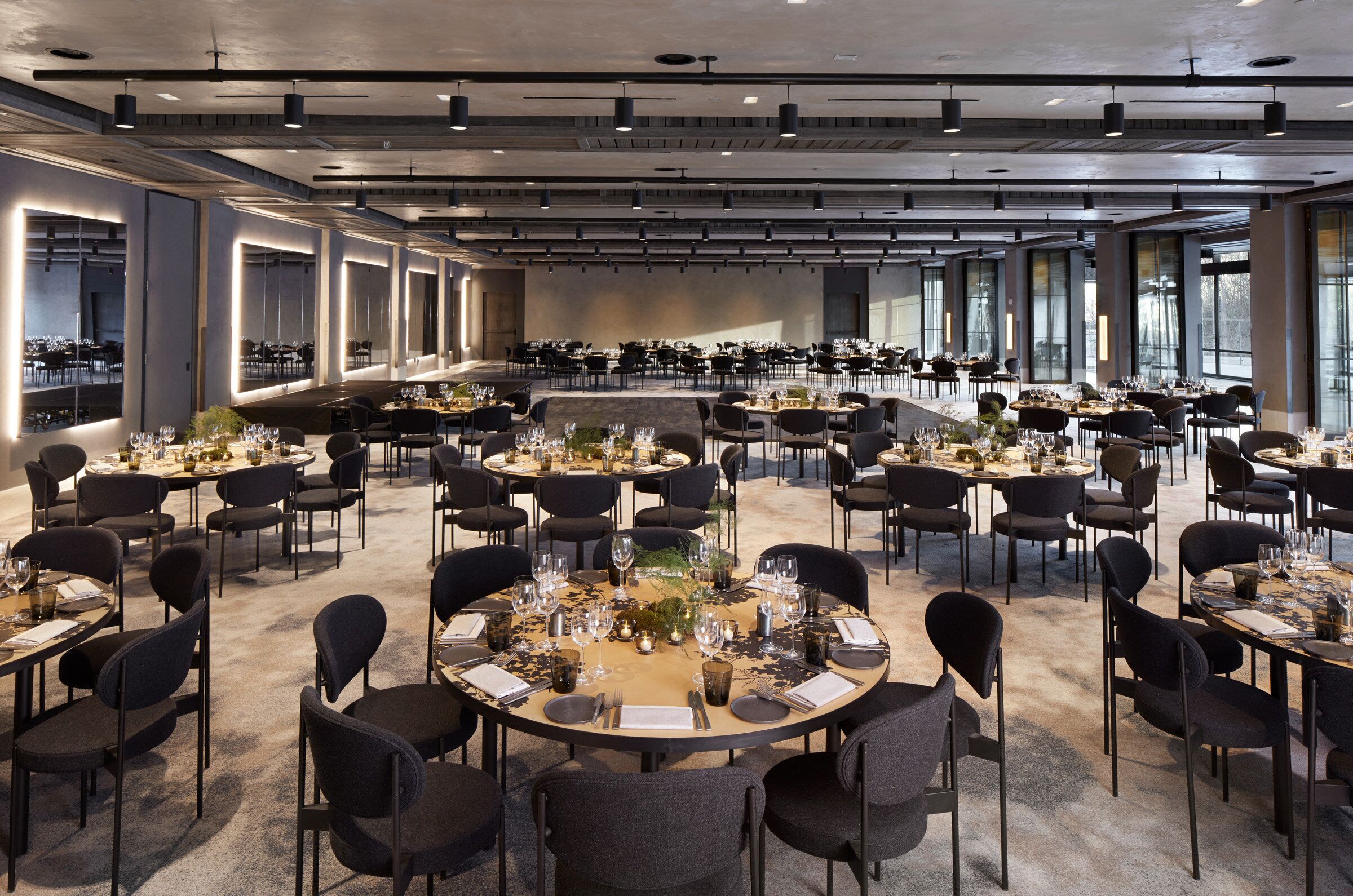 A spacious conference room with multiple tables set for dining, large windows, and a modern ceiling design.
