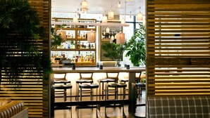 Zona de bar con listones de madera, taburetes y luces colgantes.
