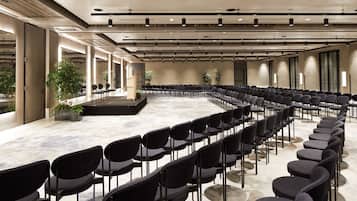 A conference room with rows of chairs, a stage, and potted plants.