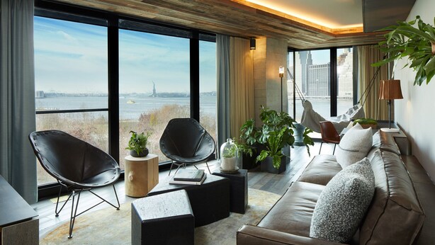 Una sala de estar moderna con un ventanal que ofrece vistas a la ciudad, un sofá, dos sillones y una mesa de centro.