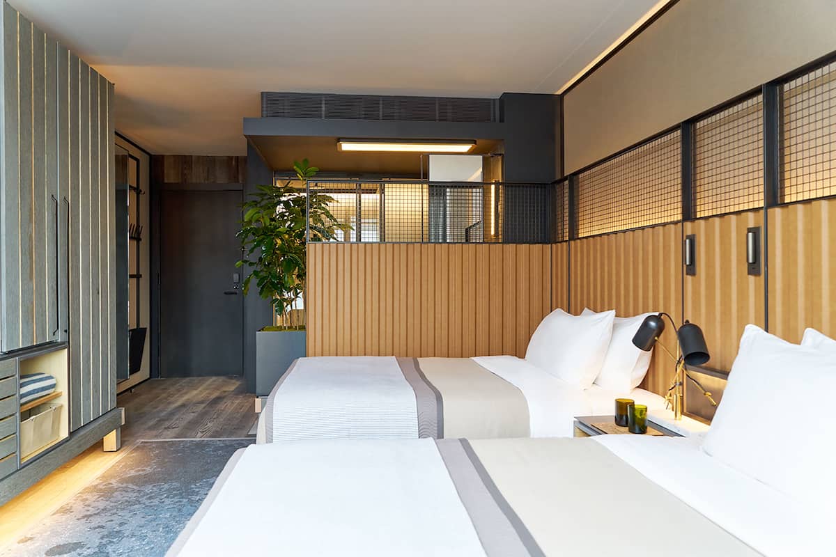 A modern hotel room with two beds, a large potted plant, and a view of the city.